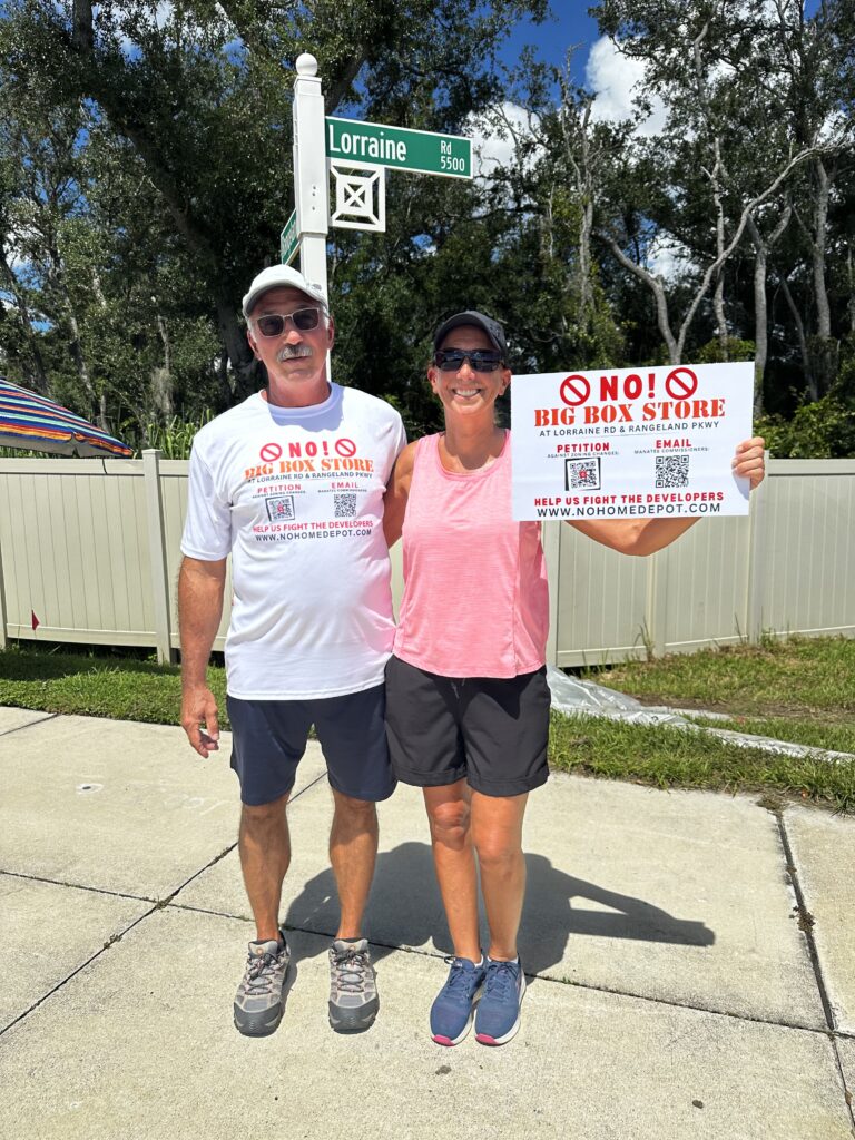 Dan Creek and Lynn Harvard standing together at the intersection of Lorraine Road and Rangeland Parkway, holding signs protesting the proposed Home Depot development.